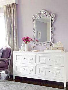 a white dresser sitting in front of a purple wall with a mirror on top of it