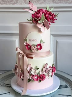 a three tiered cake with pink flowers and butterflies on the top, sitting on a table