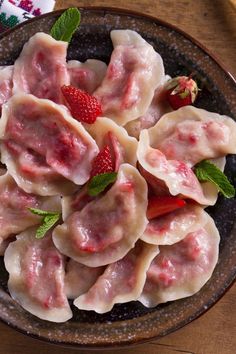 some ravioli with strawberries and mint leaves in a brown bowl on a wooden table