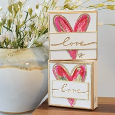 two boxes with hearts painted on them sitting next to a vase filled with white flowers