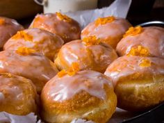 glazed doughnuts with orange zest on top in a black pan next to a glass of milk