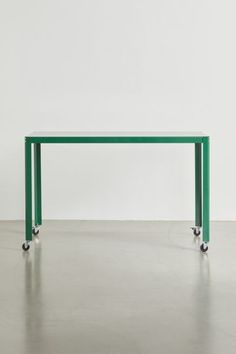 a green table sitting on top of a cement floor next to a white wall in an empty room