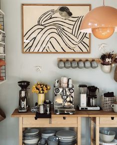 a coffee bar with plates and cups on the counter, next to an art piece