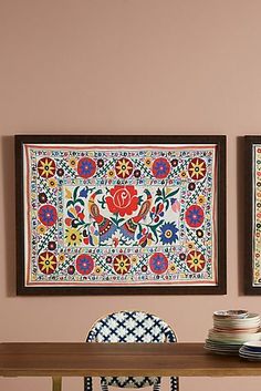 two framed pictures hang on the wall above a dining room table with chairs and plates