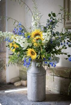 a vase filled with lots of flowers sitting on top of a cement floor next to a stone wall