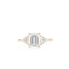 an emerald cut diamond ring with three diamonds on the band and side stones in yellow gold