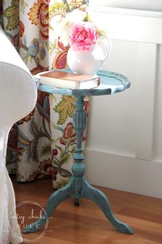 a small table with a vase on top of it next to a chair and window