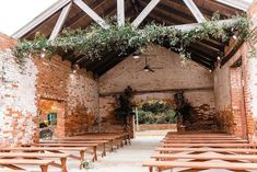 the inside of an old brick building with wooden benches and ivy growing on the roof