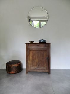 a wooden cabinet sitting in front of a round mirror on the wall next to a stool