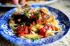 a blue and white plate topped with pasta covered in sauce, meatballs and parmesan cheese