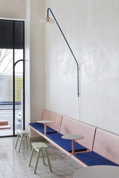 two tables and three benches in a room with white tile flooring, pink walls and blue cushions