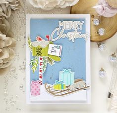 a christmas card with presents on it next to some flowers and other holiday decorations, such as pine cones