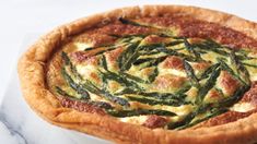 a quiche with asparagus and cheese in a pie dish on a marble surface