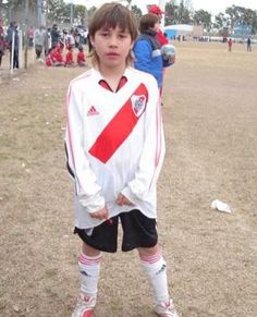 a young boy standing on top of a field wearing soccer shoes and a jersey with stripes