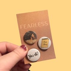 a person holding two buttons that say fearless and you're okay with the words on them