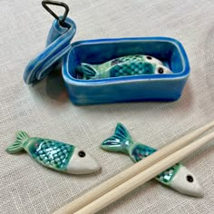 two fish figurines sitting next to chopsticks and a container on a table