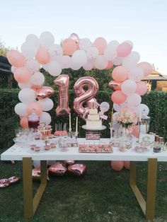 a table topped with pink and white balloons next to a large number balloon arch filled with confetti