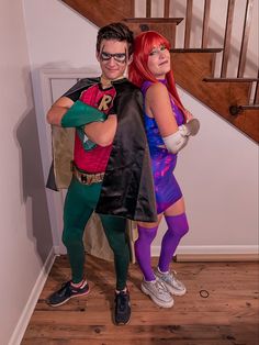 two people dressed up in costumes standing next to each other on a wooden floor with stairs behind them