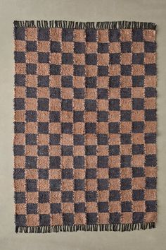 a brown and black checkered rug with fringes on the bottom, in front of a gray wall