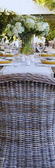 an outdoor dining area with wicker furniture and flowers in vases on the table