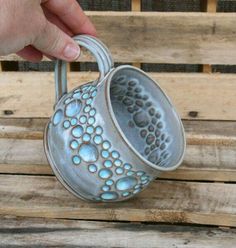 a hand holding a blue and white vase on top of a wooden bench with holes in it