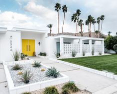 a white house with yellow doors and palm trees in the front yard on a cloudy day