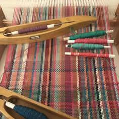 two wooden looms are sitting next to each other on a weaving mat with several different colors of yarn