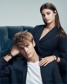 a man and woman sitting on a blue couch posing for a magazine cover photo with their arms around each other's shoulders