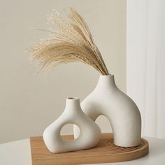 two white vases sitting on top of a wooden tray with dry grass in them