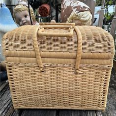 a wicker basket sitting on top of a wooden table next to a doll in the background