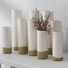 several white vases with flowers in them sitting on a shelf next to each other