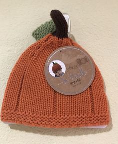 an orange knitted beanie with a green leaf on the top and a label attached to it