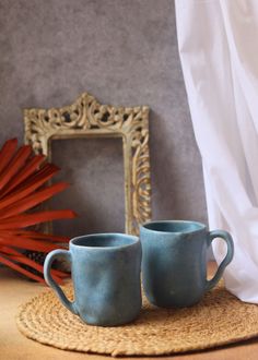 two blue mugs sitting on top of a place mat next to a framed mirror