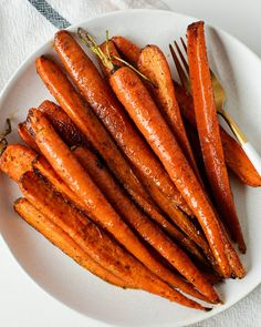 a white plate topped with cooked carrots next to a fork