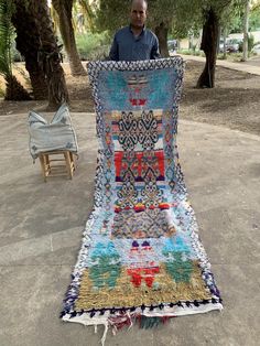 a man standing next to a very large quilt on the ground with trees in the background