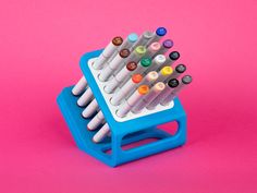 a blue and white pen holder with several pens in it on a pink background,