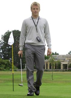 a man walking across a green covered golf course with two white flags in the background