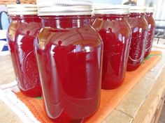 several jars are lined up on a table with an orange towel around them and one jar is filled with red liquid