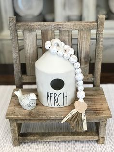 a wooden chair with a white ceramic birdhouse on it's back and beads around the neck