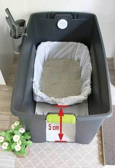 a large grey trash can with the lid down and some white flowers in front of it