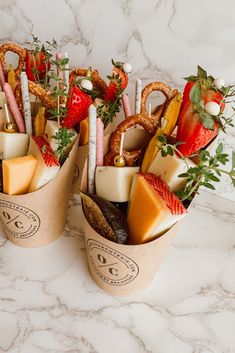 two cups filled with food on top of a white marble counter topped with strawberries and pretzels