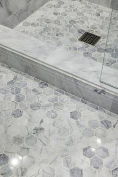 a bathroom with marble tile and hexagonal pattern on the floor, along with a glass shower door