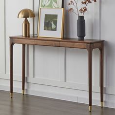 a wooden table topped with a vase filled with flowers next to a framed photograph and lamp