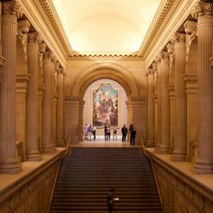 people are walking up and down the stairs in an art museum with paintings on the walls