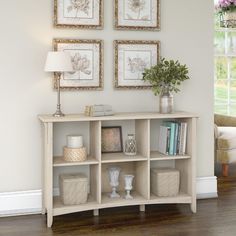 a white shelf with some pictures on the wall above it and a lamp next to it