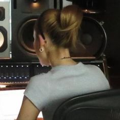 a woman sitting in front of a sound mixing desk with speakers behind her back to the camera