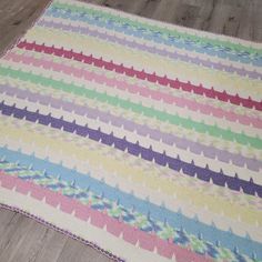 a multicolored crocheted blanket is laying on the floor next to a wooden floor