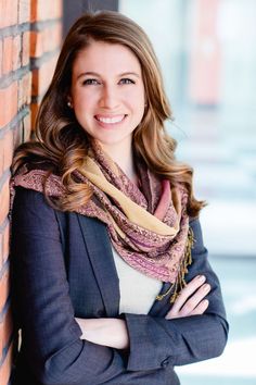 a woman standing next to a brick wall wearing a scarf and smiling at the camera