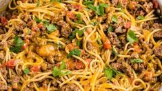 spaghetti with ground beef and cheese in a white casserole dish topped with parsley