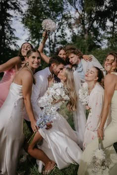 a group of people standing next to each other in front of trees and grass holding bouquets